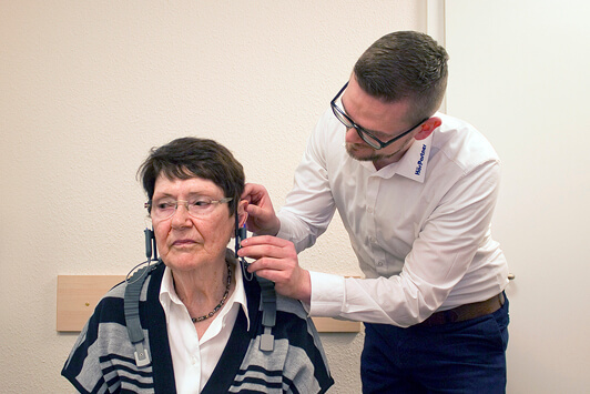 Ein Hörakustiker passt einer Seniorin im Hörtestraum ein modernes Hörgerät an.