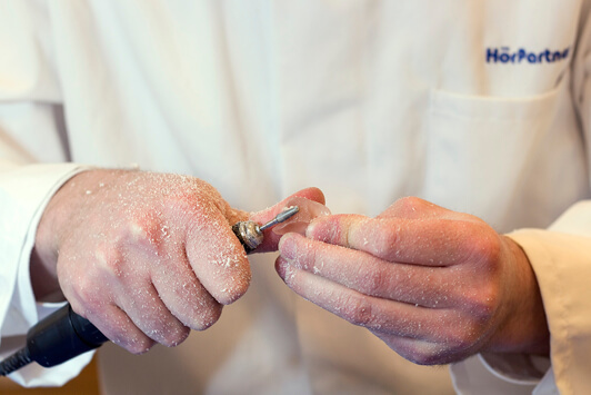 Ein Hörakustiker schleift ein Hörgerät mit einer Fräse zur individuellen Anpassung.